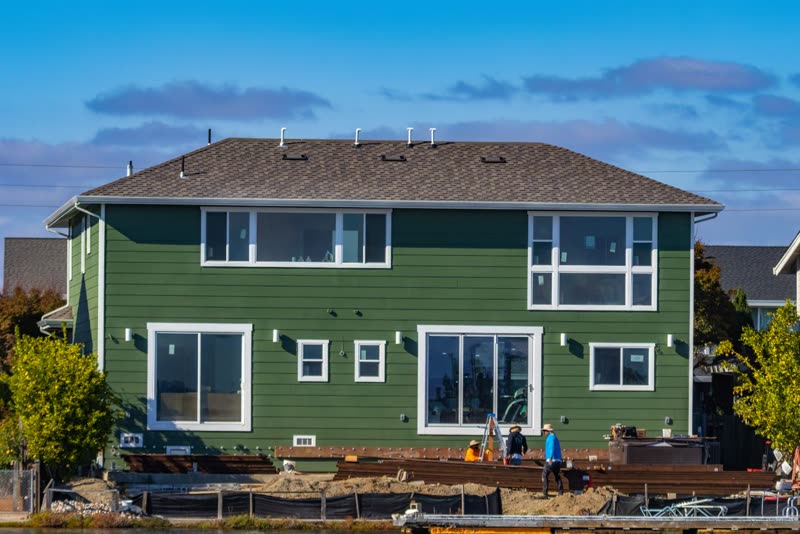 Two-storey house with new green lap siding and workers in the yard
