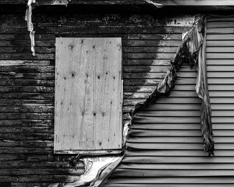 Damaged, peeling vinyl siding next to a boarded-up window